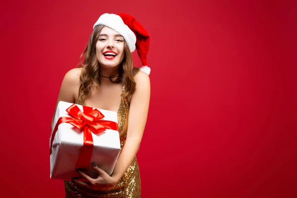 Hermosa chica sexy de Santa en oro elegante vestido de noche y sombrero de Navidad con un regalo de Año Nuevo en las manos. Emociones felicidad y deleite. Cara sonriente —  Fotos de Stock