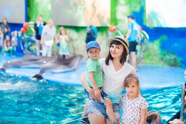 mother with children in the dolphinarium, shinochek on her arms, and the daughter is standing nearby, dolphins in the background