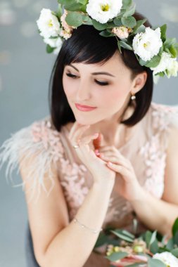 Elinde bir buket ve gri bir arka plan üzerinde kafasına çiçek bir çelenk ile güzel kız