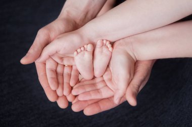 ebeveynlerin elleri yeni doğmuş bir bebeğin ayaklarını tutun, avuçiçlerinde pembe topuklu, ebeveyn sevgisi