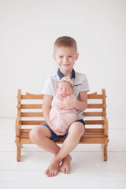 Ağabeyi elinde pembe bir kozanın içinde yeni doğmuş bir kız kardeşi tutuyor ve tahta bir bankta oturuyor, abi kardeş, kardeş sevgisi