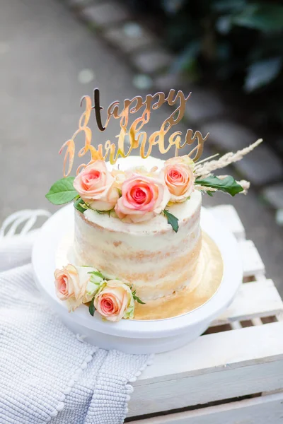 Çok güzel bir sünger doğum günü pastası. Doğada beyaz bir kutuda altın harfler, güller ve çiviler var.