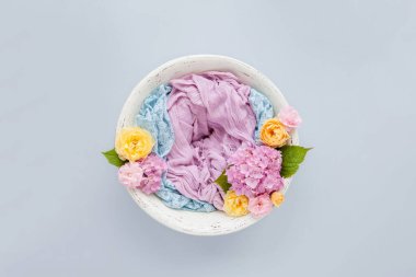 Beyaz ahşap bir kâse içinde pembe ve mavi bir bez ve pembe ortancalarla mavi arka planda sarı güller olan yeni doğmuş bir bebeğin fotoğraf çekimi için arka plan