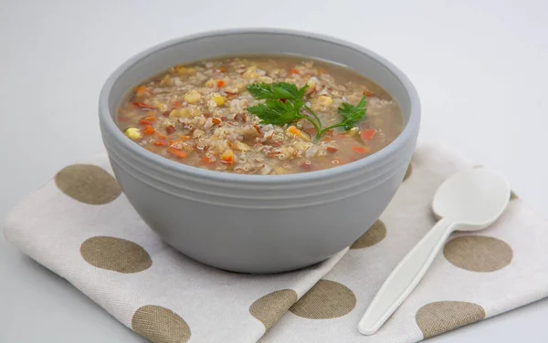 Peruvian quinoa soup with red rice and lentils in a gray clay bowl garnished with a leaf of green parsley