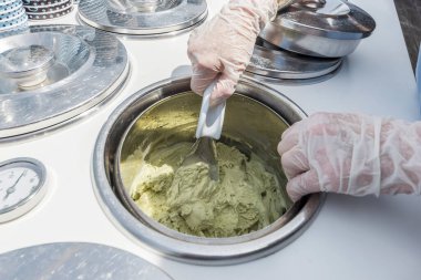 Şam fıstıklı dondurmayı inoks kasesinde karıştırıyor.