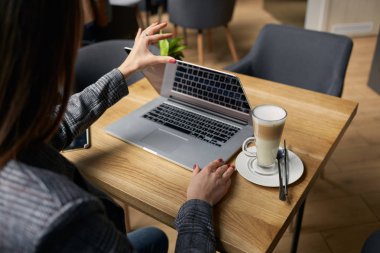 Yaşam tarzı eğitim öğrencisi. Businesswoman proje için laptop üzerinde çalışır. Millennial evde ofis içecek kahve defter üzerinde iş arıyor. Modern taşınabilir bilgisayar ve telefon kullanarak tanınmaz kadın