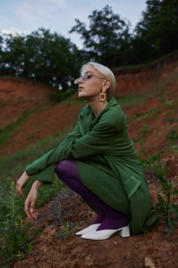 Yeşil ceket ve güneş gözlüğü ile tepede güzel bir kız. Moda portresi