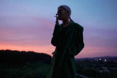 Yeşil ceket ve güneş gözlüğü ile tepede güzel bir kız. Moda portresi