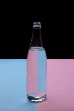 Parlak pembe ve mavi arka planda cam şişe su yakın