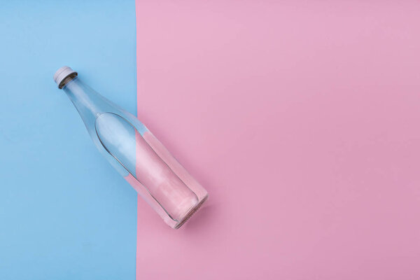 Вода из стеклянной бутылки на ярко-розовом и синем фоне
