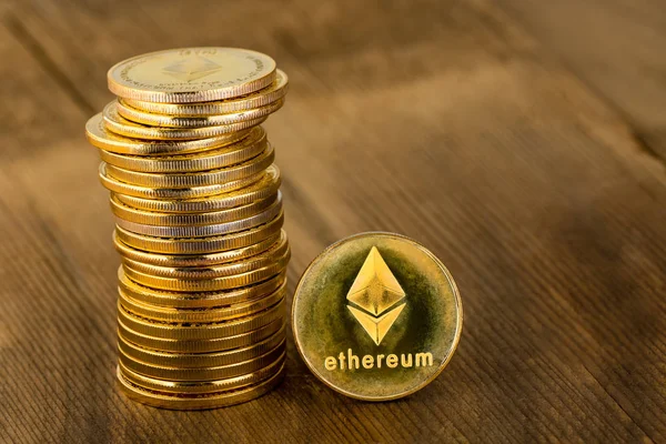 Pile of golden coins with Ethereum logo in close-up on wooden table with copy space