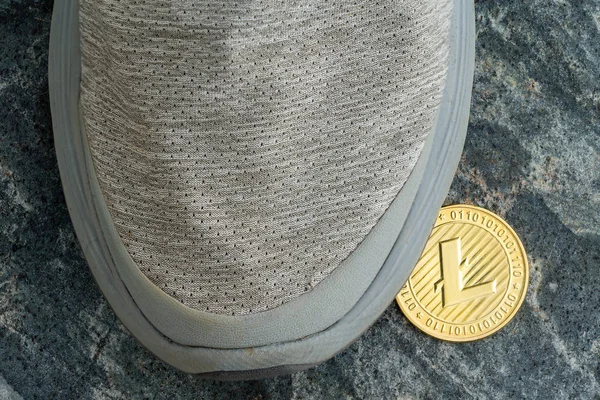 Single gold Litecoin left under a grey shoe on a grey textured stone floor viewed from above in a concept of digital finances and cryptocurrencies