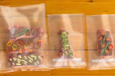 Vacuum packed flat iron steaks for freezing ready for sous-vide cooking with three different savory seasonings on a wooden board clipart
