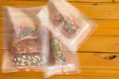 Multiple random meat dishes with bits of vegetables inside plastic bags sitting on wooden plank table clipart