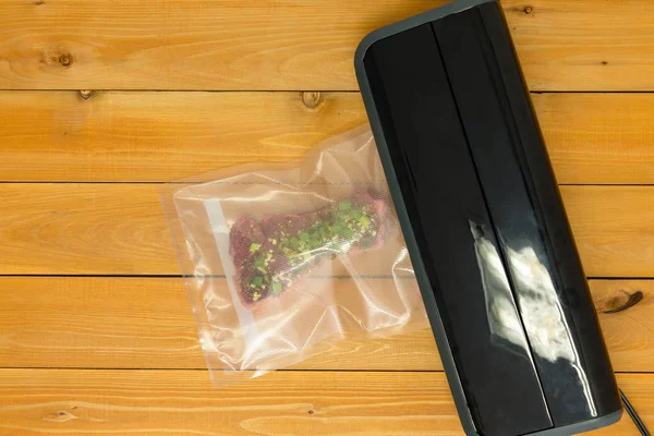 Sealing a vacuum packed flat iron steak in clear plastic for freezing or sous-vide cooking on a heated appliance viewed from above on a wooden table