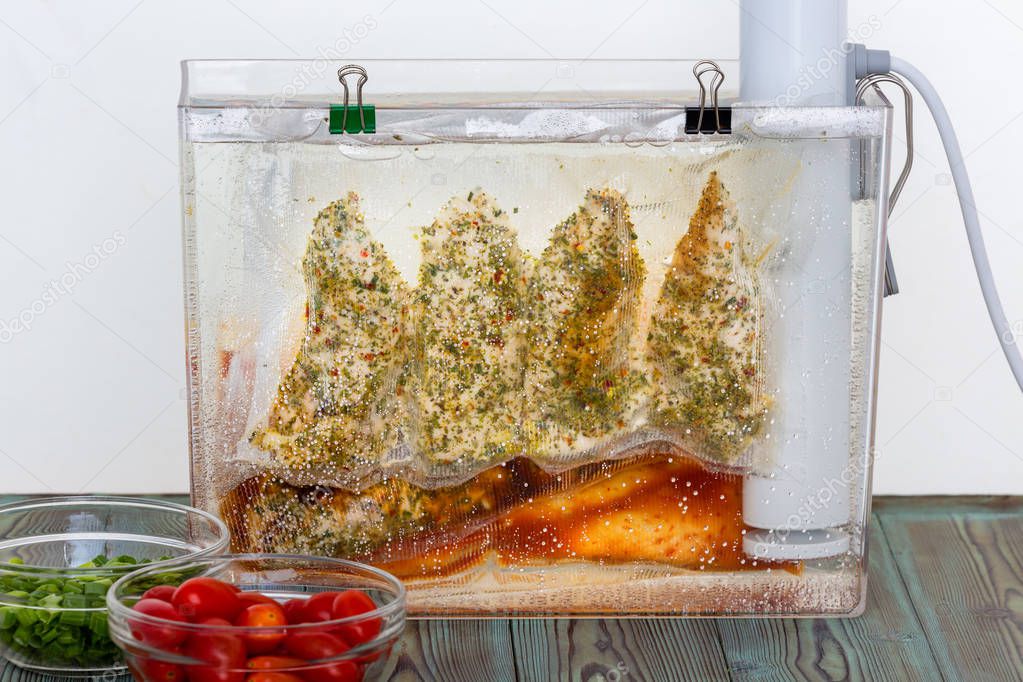 Three bags of chicken breasts with assorted marinades and seasoning hanging suspended in water sous-vide cooking at an even temperature