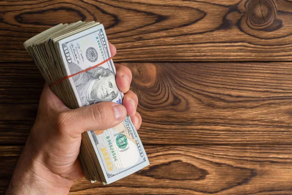 Adam bir rustik ahşap arka plan kopya alanı ile üzerinde 100 dolar faturaları veya Benjamins kalın bir yığın elinde sürükleyici
