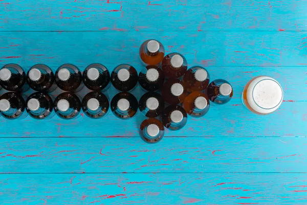 矢印をコピー スペースを持つエキゾチックなターコイズ ブルーのクラックル ペイント背景に泡状の頭を持つラガーの完全パイント グラスを指しているビール瓶の形成 — ストック写真