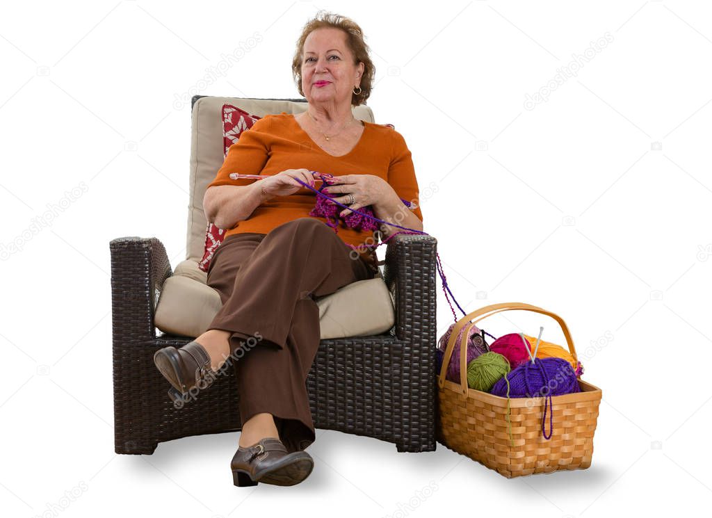 Happy elderly lady relaxing in a wicker chair with her knitting and a basket of colorful balls of wool alongside her on a white background with copy space