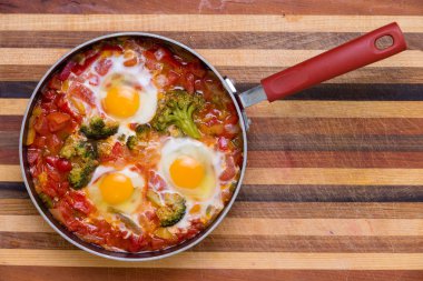 Bir tavada kopya alanı ile yukarıdan izlendi lezzetli baharatlı geleneksel shakshuka brokoli ve lamine ahşap tahta üzerinde haşlanmış yumurta ile hizmet