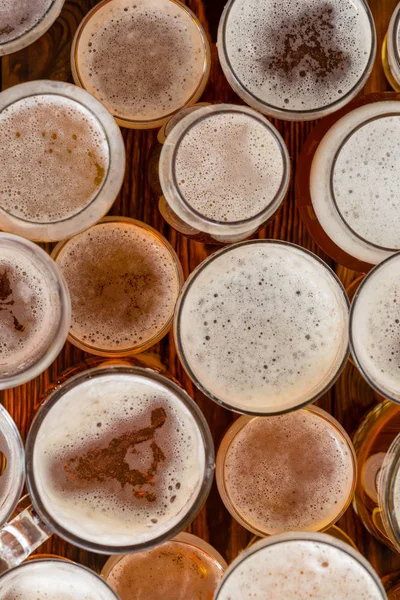 An variety of full, frothy beer glasses and sizes on a bar bench top.