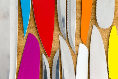 Flat lay background of the blades of assorted old sharpened steel and ceramic knives laid tip to tip on rustic wood viewed close up from above clipart
