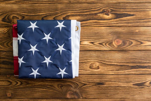 Neatly folded American flag showing the stars representing the original 13 colonies on a wooden table viewed from overhead with copy space