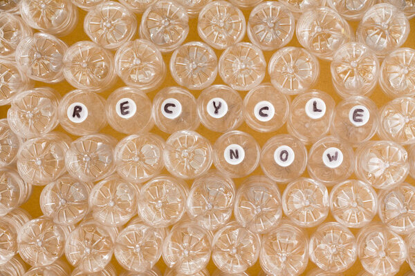 Multiple clean plastic bottles ready to be recycled viewed upended except for a few with the handwritten message - Recycle Now - handwritten on the white caps in a full frame conceptual image