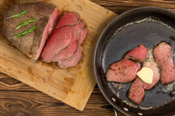 調理した肉ステーキと木製のテーブルの上にバターの正方形を保持している黒のパンの横にまな板の上のスラブ — ストック写真