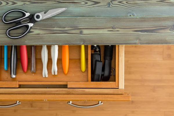 Neat line of colorful knives in a fitted drawer in a wooden kitchen cabinet with rustic counter top viewed from overhead with a pair of scissors or shears on top