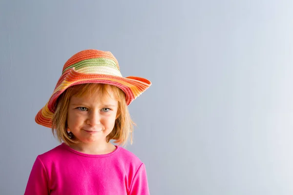 鮮やかなピンクのドレスとカラフルな麦わら帽子の若いブロンドの女の子 コピー スペース プレーンの灰色の背景に対してフロント バストの肖像画 — ストック写真