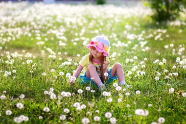 Şapkalı kız bir cephede oturur ve bir karahindiba keser