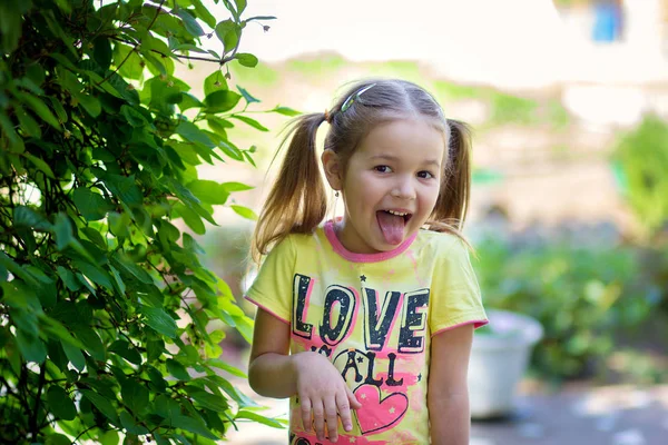 小女孩花费在绿色灌木附近并且伸出舌头 — 图库照片