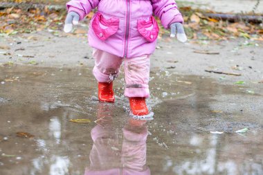 Pembe bir ceket çocuk havuzları üzerinde sonbaharda kırmızı gumboots yürür