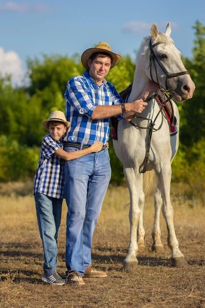 男子与儿子在帽子和蓝色衬衫行走与白马 — 图库照片