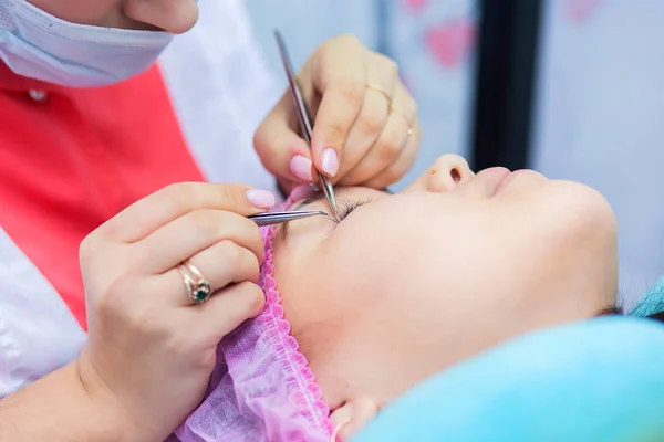 The master in eyelash extension works in beauty shop with the client. The girl increases eyelashes