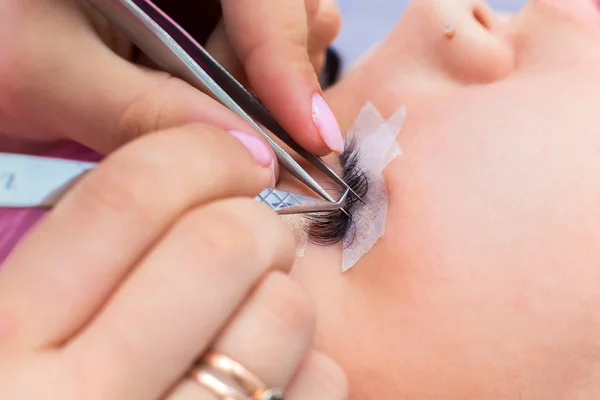 The master in eyelash extension works in beauty shop with the client. The girl increases eyelashes
