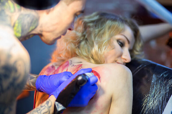 Парень делает татуировку девушке в тату-салоне.
