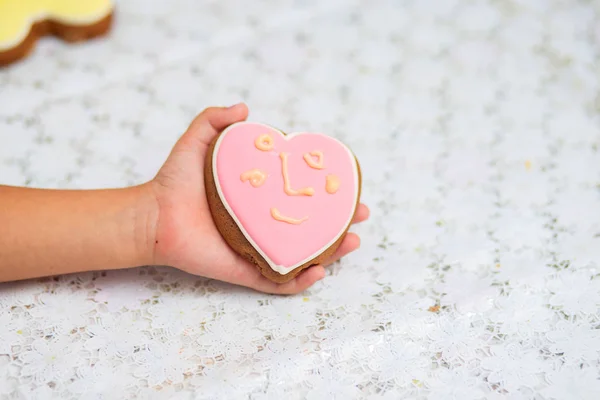 Pink Cookies in the form of heart lie on a children's hand. The child decorated cookies with cream independently. Children's drawing