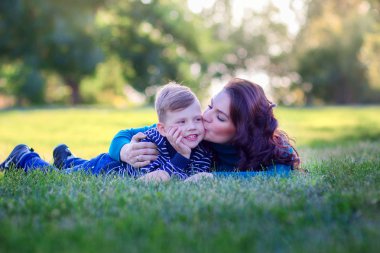 Genç anne kucaklayan, parkta bir çim üzerinde yalan oğlu kisses