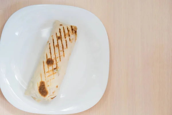 A porção de shawarma em um lavash está em uma placa branca em uma mesa de madeira — Fotografia de Stock