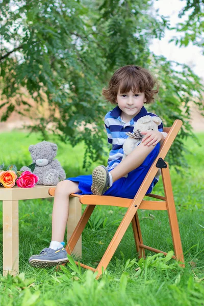 El chico con una camiseta azul a rayas se sienta en un taburete al aire libre entre greens — Foto de Stock
