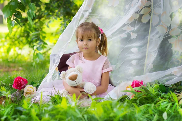 Het meisje in een elegante jurk zit met een teddybeer in een tent buitenshuis — Stockfoto