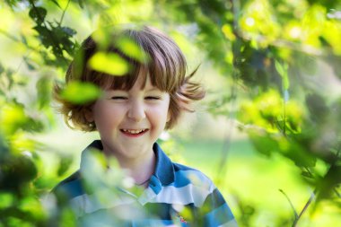 Kıvırcık saçlı neşeli çocuk gülen ve ağaç dalları gizler
