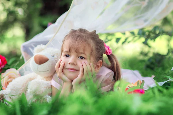 Het kleine meisje poseert buiten liggend met een teddybeer — Stockfoto