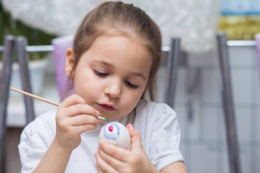 Kız mutfakta oturur ve Paskalya için bir yumurta fırçası ile boyar