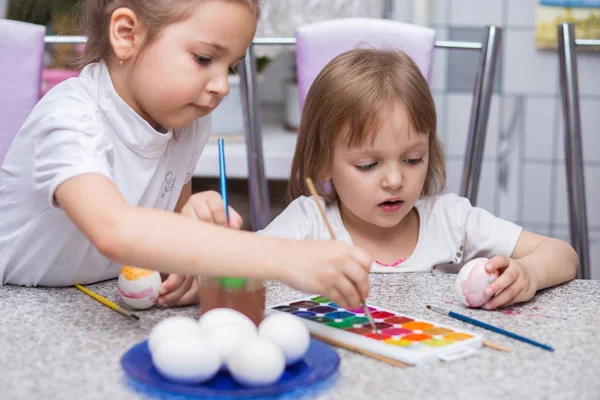 Two sisters stay at home in kitchen and paint eggs for Easter with watercolor paints — Stock Photo, Image