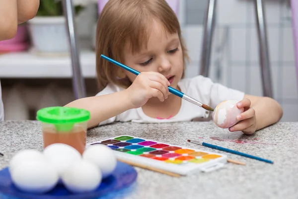 A menina em casa na cozinha pinta ovos de Easter com uma escova e pinturas de aquarela — Fotografia de Stock