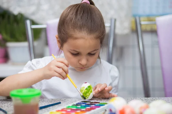 Девушка сидит на кухне и рисует акварельные краски на пасхальном яйце — стоковое фото