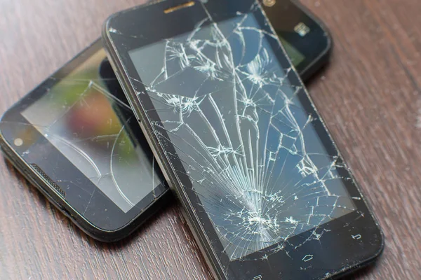 Two broken black smartphones lie the friend on the friend on a wooden background.